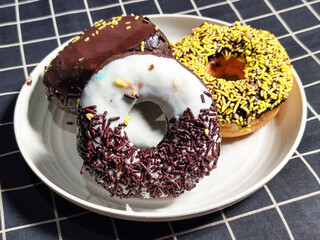 Three delicious donuts topped with sprinkles and various colored glazes, displaying a tempting...