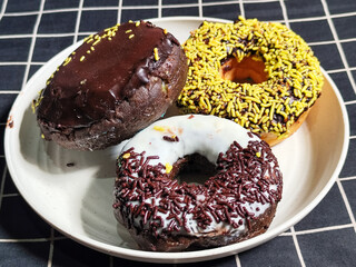 Three delicious donuts topped with sprinkles and various colored glazes, displaying a tempting...