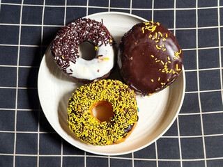 Three delicious donuts topped with sprinkles and various colored glazes, displaying a tempting...