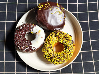 Three delicious donuts topped with sprinkles and various colored glazes, displaying a tempting...