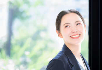 メインビジュアルにも綺麗な柔らかい新緑の中でパソコンを持つスーツの女性のビジネスシーン　クローズアップ　振り返る