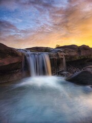 a waterfall that flows between black rocks and is illuminated by the afternoon sun
