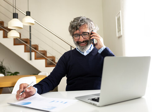 Happy mature man talking on the phone laughing at home office - Powered by Adobe