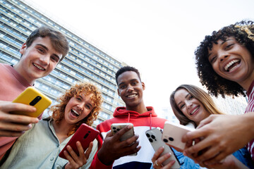 Obraz premium Happy students using smartphones in university campus: low angle view of cheerful diverse friends enjoying mobile technology