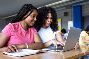 Two female college students collaborating on a project using laptop in library