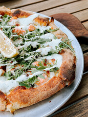 Succulent pizza topped with greens and lemon served on a wooden table