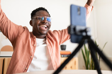 Influencer raising arms while streaming live with smartphone on tripod