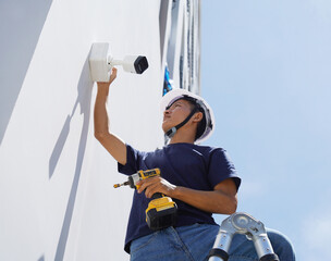 A technician installs a CCTV camera on the facade of a residential building