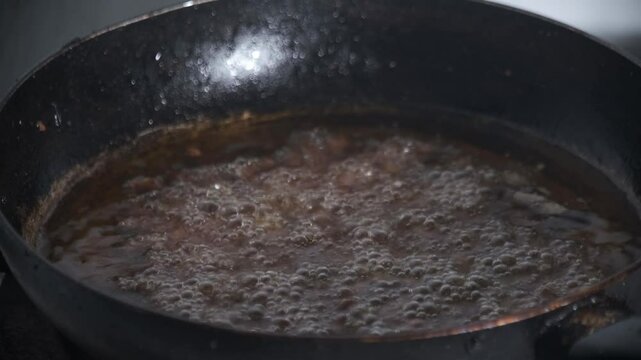Hot oil bubbles in a black pan while frying peanuts, creating an authentic cooking scene. The sizzling foam and golden texture highlight the frying process, representing traditional food preparation. 