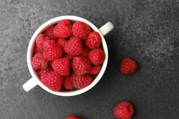 Raspberries in cup on black textured background for gourmet snack or modern food styling concept