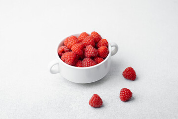 Bowl of fresh raspberries with scattered berries for snack or breakfast concept