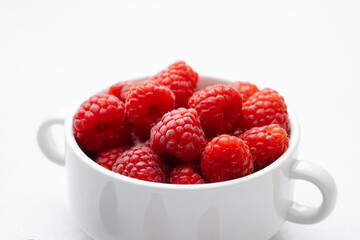Bowl of fresh raspberries with scattered berries for snack or breakfast concept