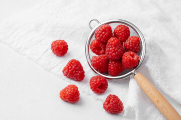 Raspberries in strainer with scattered berries for snack prep or summer dessert concept