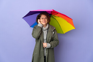 English woman holding an umbrella isolated on purple background frustrated and covering ears