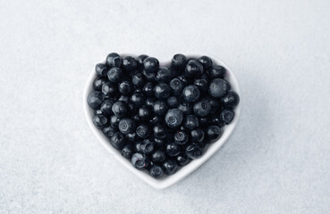Blueberries in heart-shaped bowl on white for health, love or superfood concept