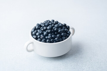 Blueberries in white bowl on light background for breakfast, diet or wellness concept