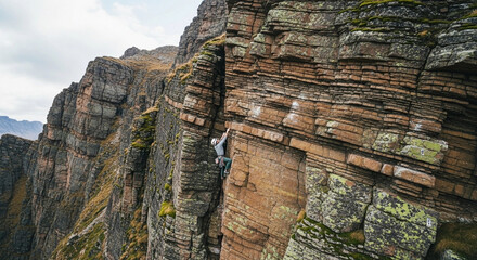 A rock climber ascending a steep, layered cliff face, reaching upwards.