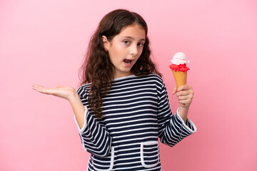 Little caucasian girl holding an ice cream isolated on pink background with shocked facial...