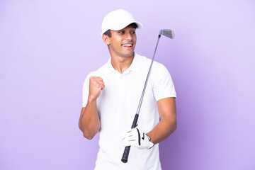 Young caucasian man isolated on purple background playing golf and celebrating a victory