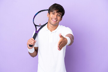 Handsome young tennis player man isolated on ocher background shaking hands for closing a good deal