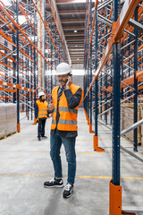 Warehouse manager talking on smartphone, coordinating logistics and managing inventory inside a...