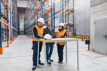 Warehouse workers and manager analyzing data on a digital tablet, optimizing logistics and...