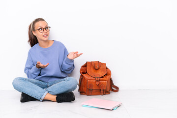Young student girl sitting one the floor isolated on white background with surprise facial...