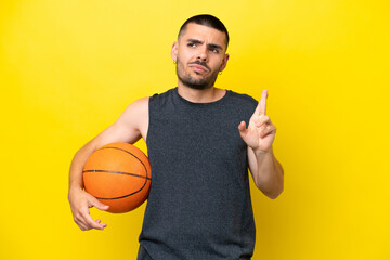 Young caucasian basketball player man isolated on yellow background with fingers crossing and...