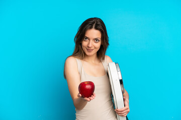 Young caucasian woman isolated on blue background holding weighing machine and offering an apple