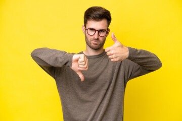 Young caucasian man isolated on yellow background making good-bad sign. Undecided between yes or not
