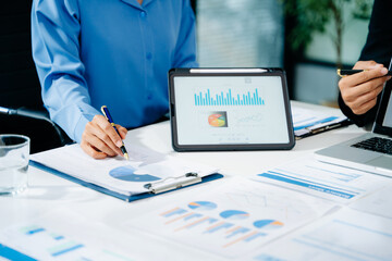 Business documents on office table with smart phone and laptop and two colleagues discussing data in the background