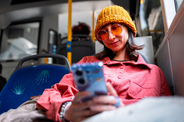 Portrait of beautiful young girl using smartphone while sitting alone in bus. Woman using public...
