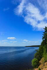 Peaceful coastal landscape with blue sky, scattered clouds, and calm water beside a forested shoreline