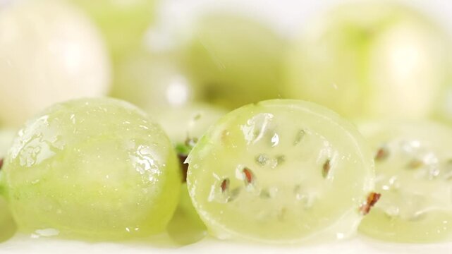 Macro shot of a halved gooseberry with water droplets falling on it, showcasing its natural texture and vibrant color. Ideal for health, food, and nature-related projects