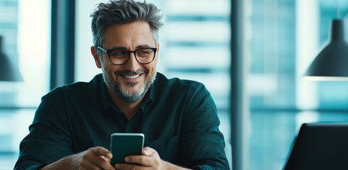 Professional middle aged man smiling while using mobile phone in modern office setting. atmosphere is bright and inviting, showcasing blend of technology and comfort