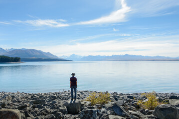 Man standing on the rocks by Lake Pukaki, enjoying the views of Mt Cook and Southern Alps. South...