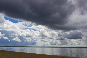 Dramatic cloudy sky over a calm lake with a sandy shoreline and distant horizon