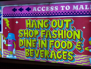 A colorful and eye-catching sign directing visitors to a mall for various activities like hanging...