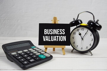 Business Valuation text with alarm clock on wooden background