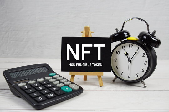 NFT abbreviation of Non Fungible Token text with alarm clock on wooden background