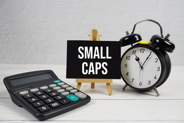 Small Caps text with alarm clock and calculator on wooden background