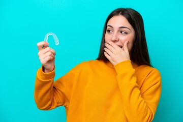 Young caucasian woman holding invisible braces isolated on blue background with surprise and...