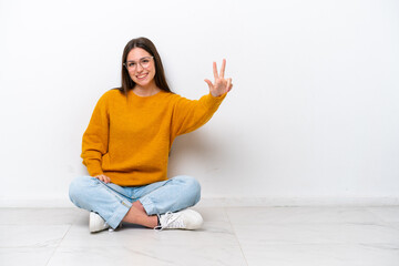 Young girl sitting on the floor isolated on white background happy and counting three with fingers