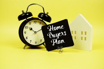 Home Buyers' Plan text with alarm clock and house model on yellow background
