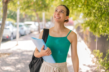 Young pretty student woman at outdoors looking up while smiling