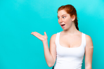 Young reddish woman wearing a band aids on blue background with surprise facial expression
