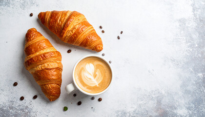 Minimalist flat lay of a fresh croissant and a latte with beautiful foam art on a light-textured stone background.