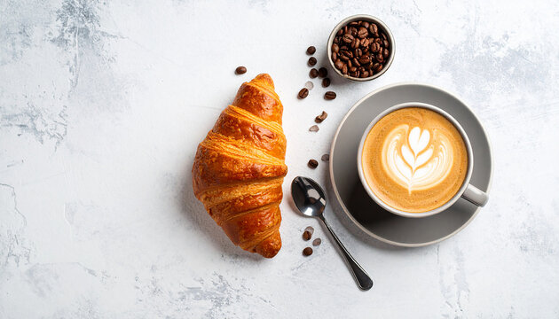 Minimalist flat lay of a fresh croissant and a latte with beautiful foam art on a light-textured stone background.