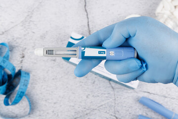 Healthcare concept with semaglutide pen held by gloved hand on concrete background, clean top view for pharmaceutical content