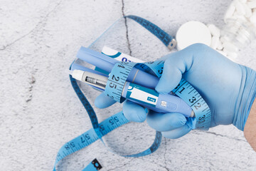Blue gloved hand holding semaglutide pen and measuring tape on concrete surface, top view concept for diabetes care and obesity treatment